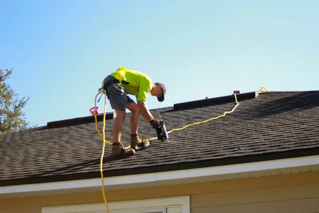 A roofer at work on a shingle roof