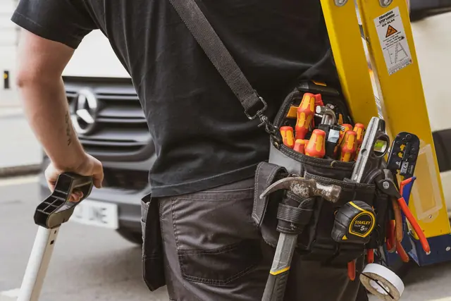 A contractor wearing a tool belt beside a work truck